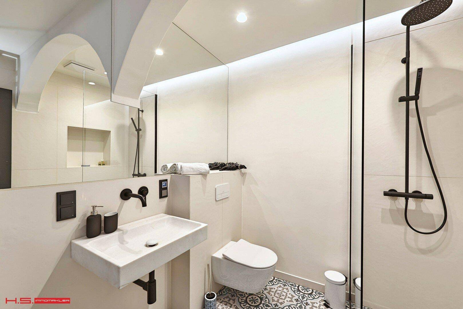 Modernes Badezimmer mit wandhängendem WC, Waschbecken, großem Spiegel und begehbarer Dusche.