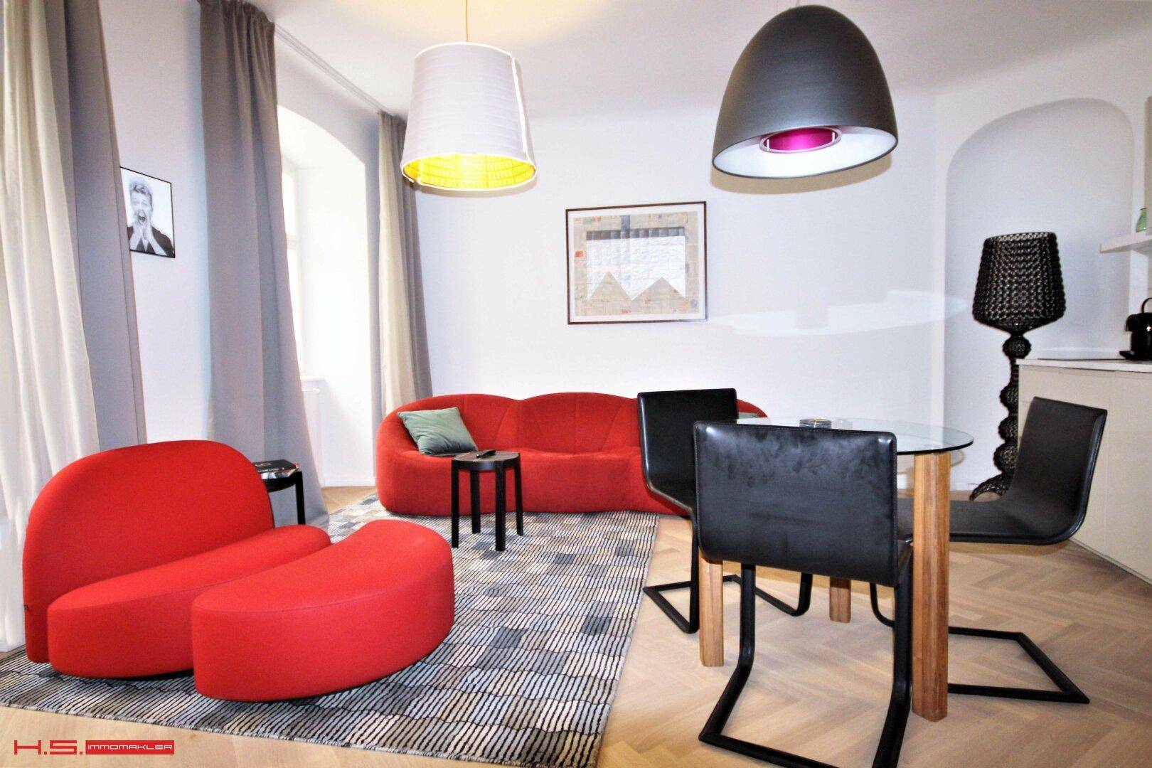 Gemütlicher Wohnbereich mit rotem Sofa, Esstisch und Fischgrätparkett, hell und modern eingerichtet.