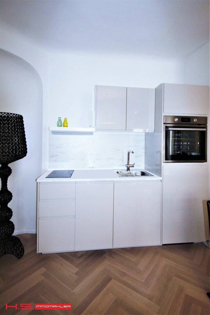 Moderne Küchenzeile mit weißen Schränken, Spüle und Induktionskochfeld auf Fischgrätparkett.