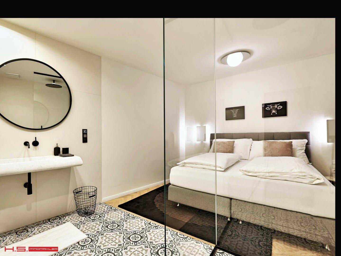 Schlafzimmer mit Doppelbett und offenem Badezimmerbereich, getrennt durch eine Glaswand.