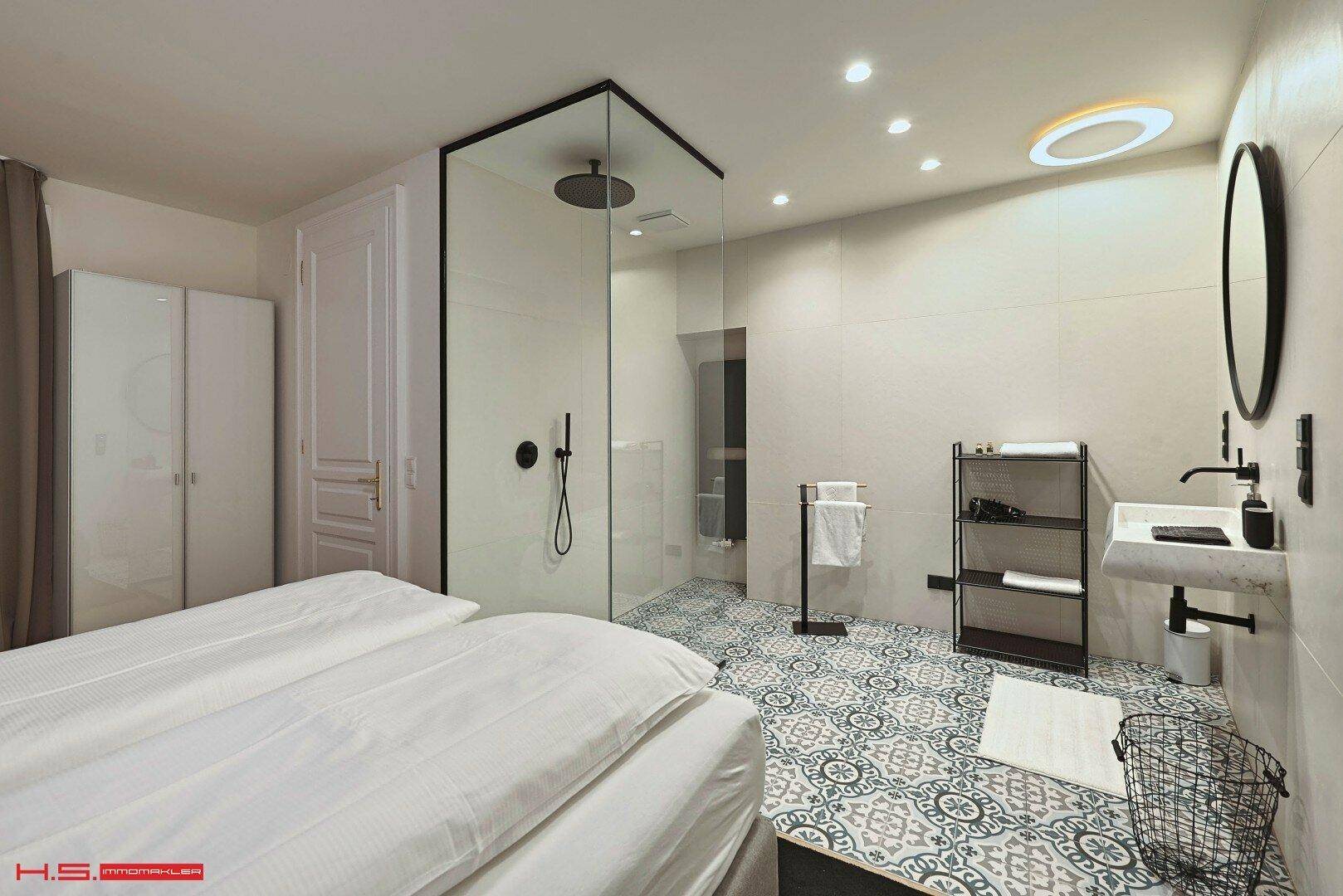 Schlafzimmer mit integriertem Badezimmer, begehbarer Dusche und stilvollen gemusterten Bodenfliesen.