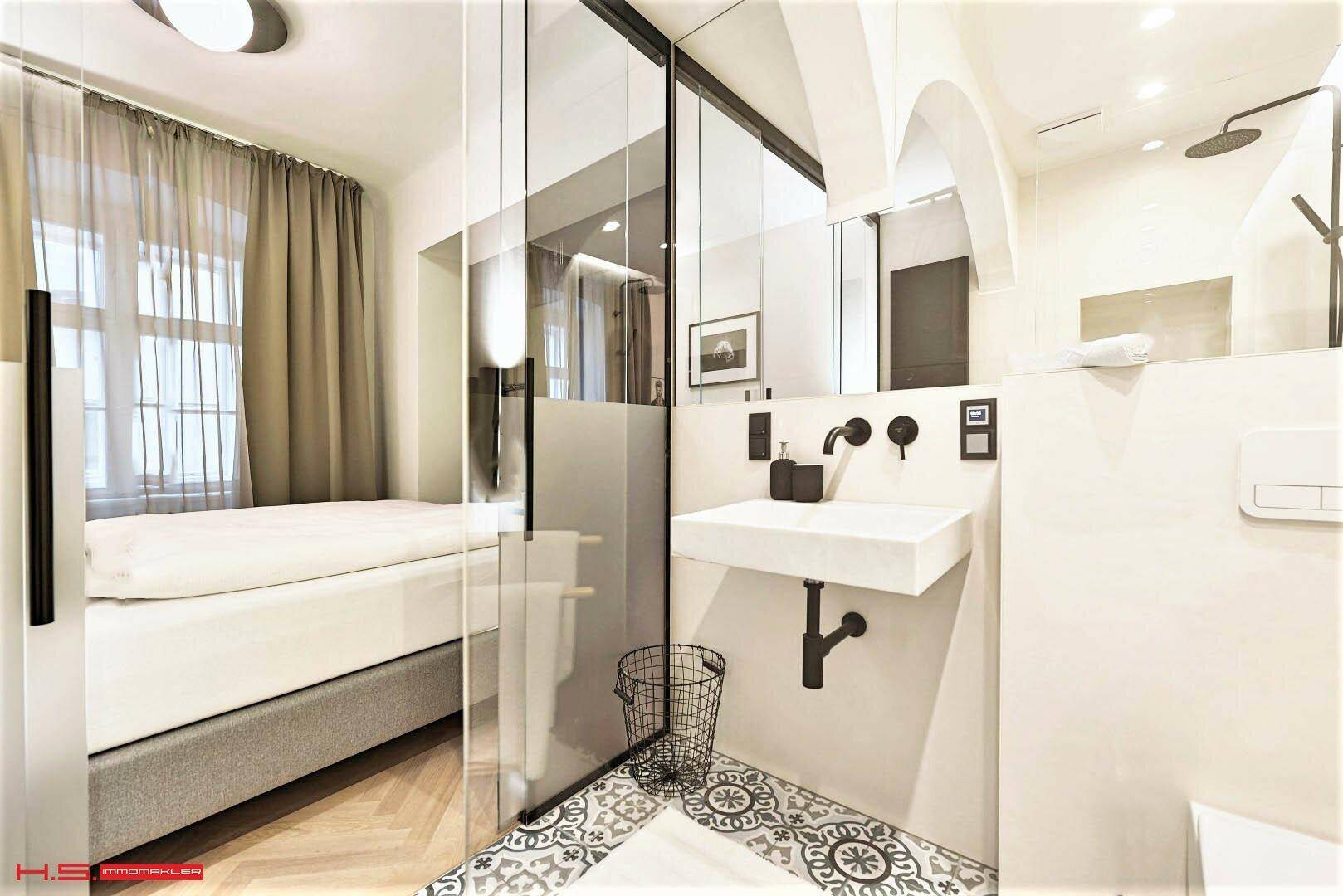 Modernes Badezimmer mit Waschbecken und Blick ins Schlafzimmer durch eine elegante Glasabtrennung.