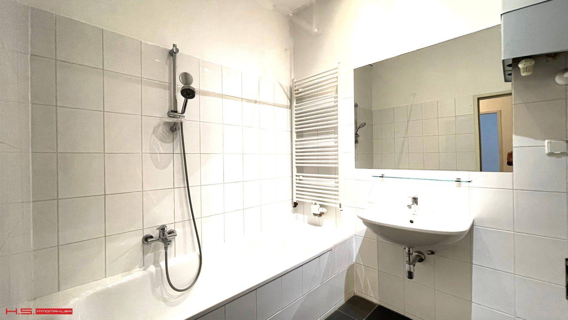 Helles Badezimmer mit weißen Fliesen, Badewanne und beheiztem Handtuchhalter.