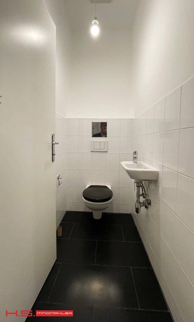 Kleines Gäste-WC mit Wand-WC, Waschbecken und dunklem Fliesenboden.