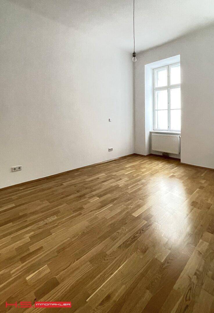 Lichtdurchfluteter Raum mit glänzendem Parkettboden und hohen Fenstern.