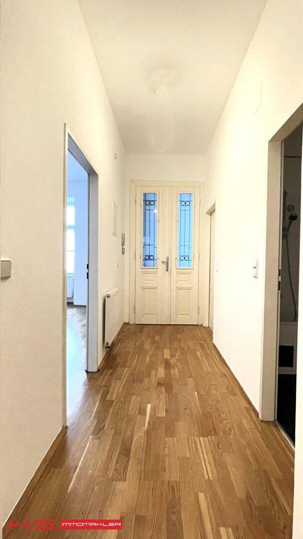 Langer, heller Flur mit Parkettboden und einer verzierten Eingangstür.