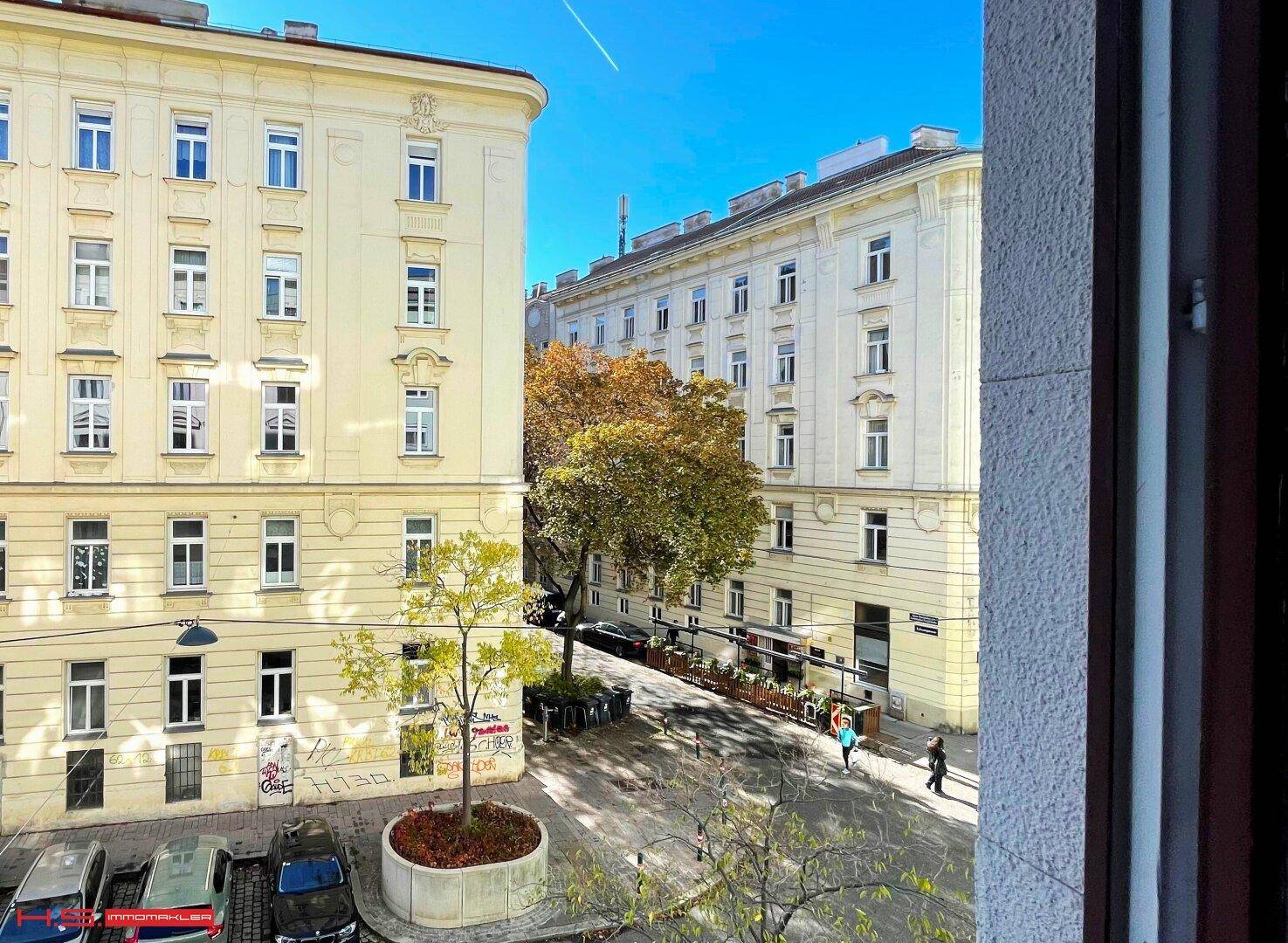 Blick aus dem Fenster auf eine belebte Straße mit Bäumen und umliegenden Gebäuden.