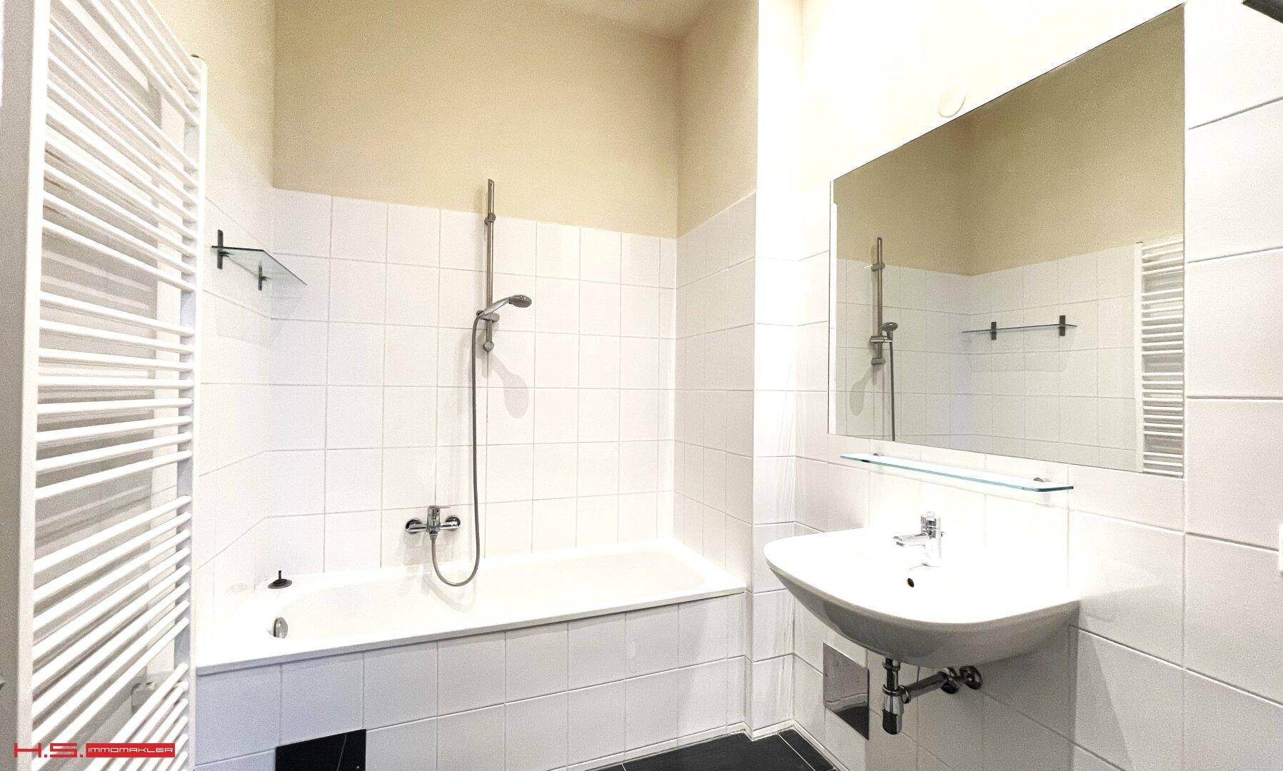 Modernes Badezimmer mit weißen Fliesen, Badewanne mit Duschfunktion und Handtuchheizkörper.