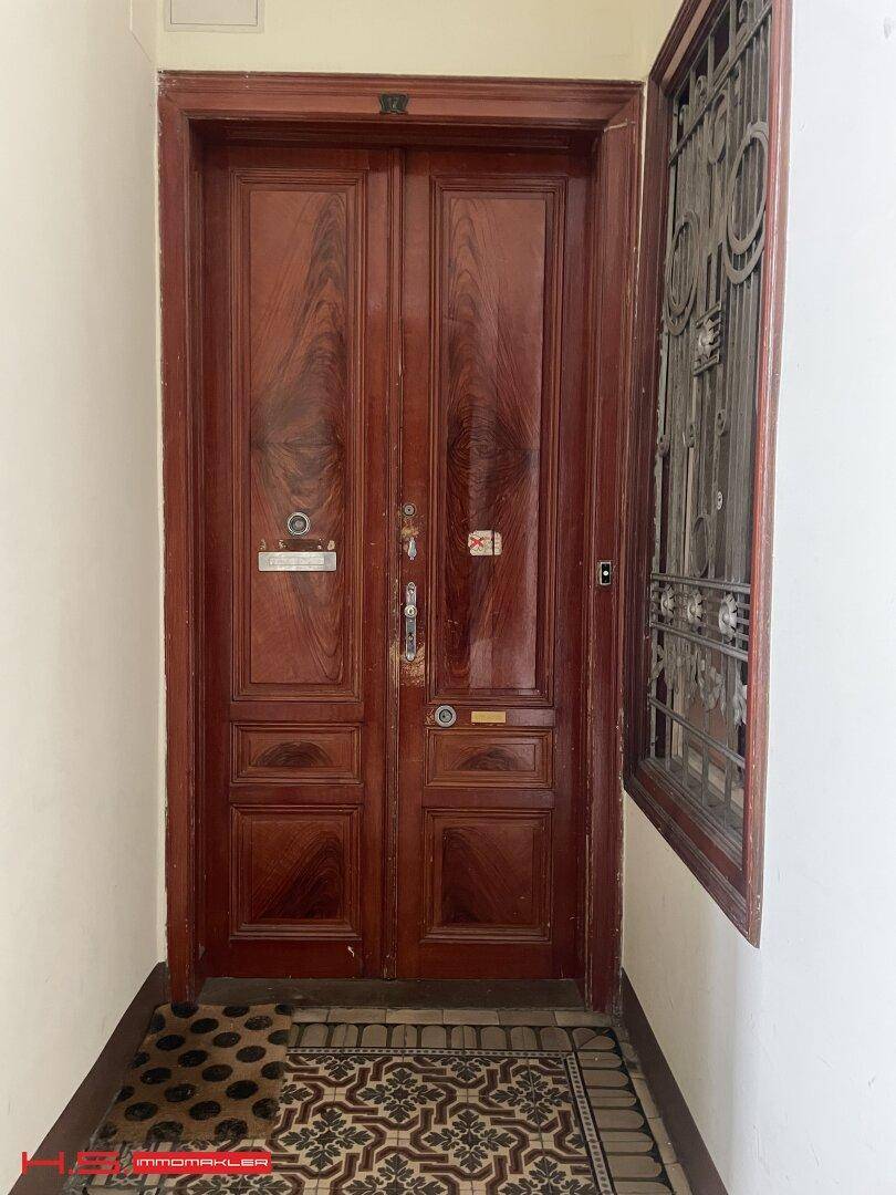 Elegante Eingangstür aus Holz mit kunstvollen Verzierungen und historischen Fliesen im Eingangsbereich.