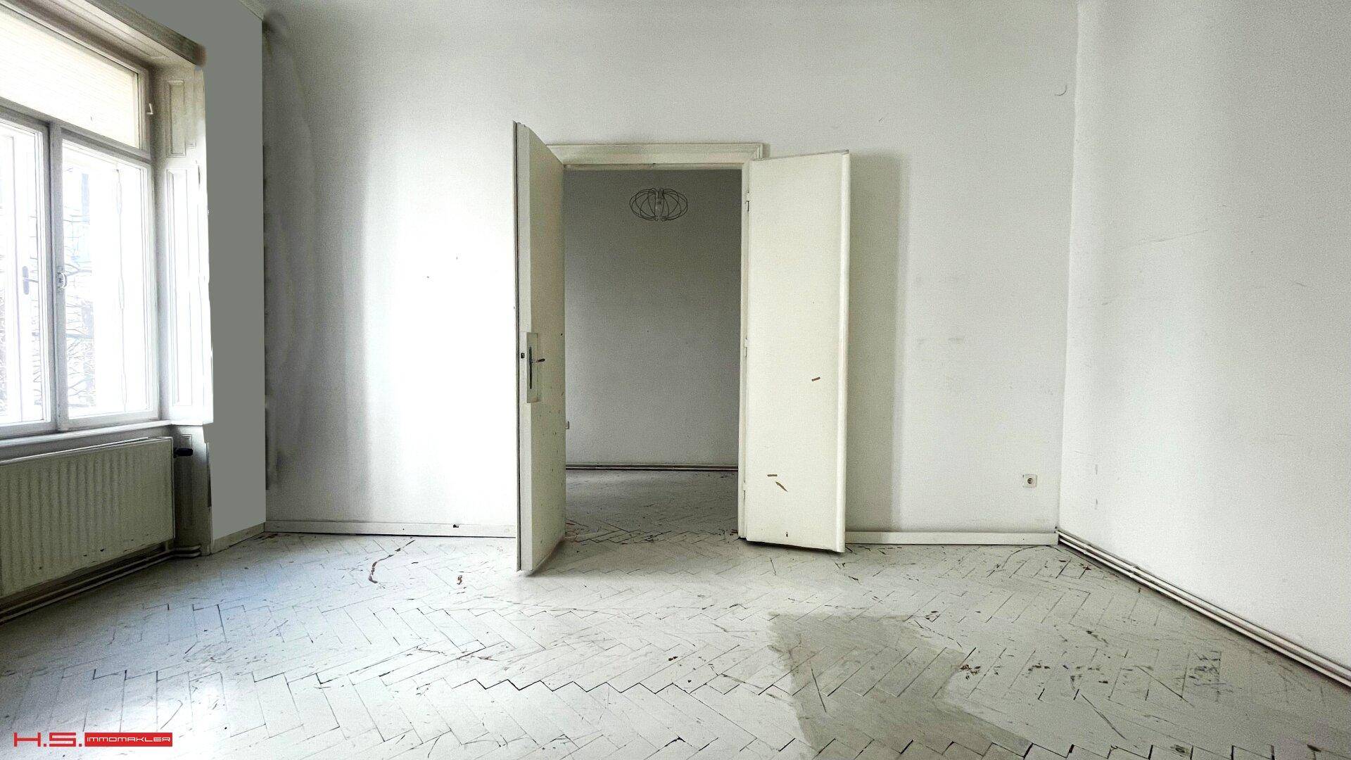 Geräumiges Zimmer mit weiß gestrichenem Fischgrätparkett und hohen Türen, ideal für Schlaf- oder Arbeitszimmer.