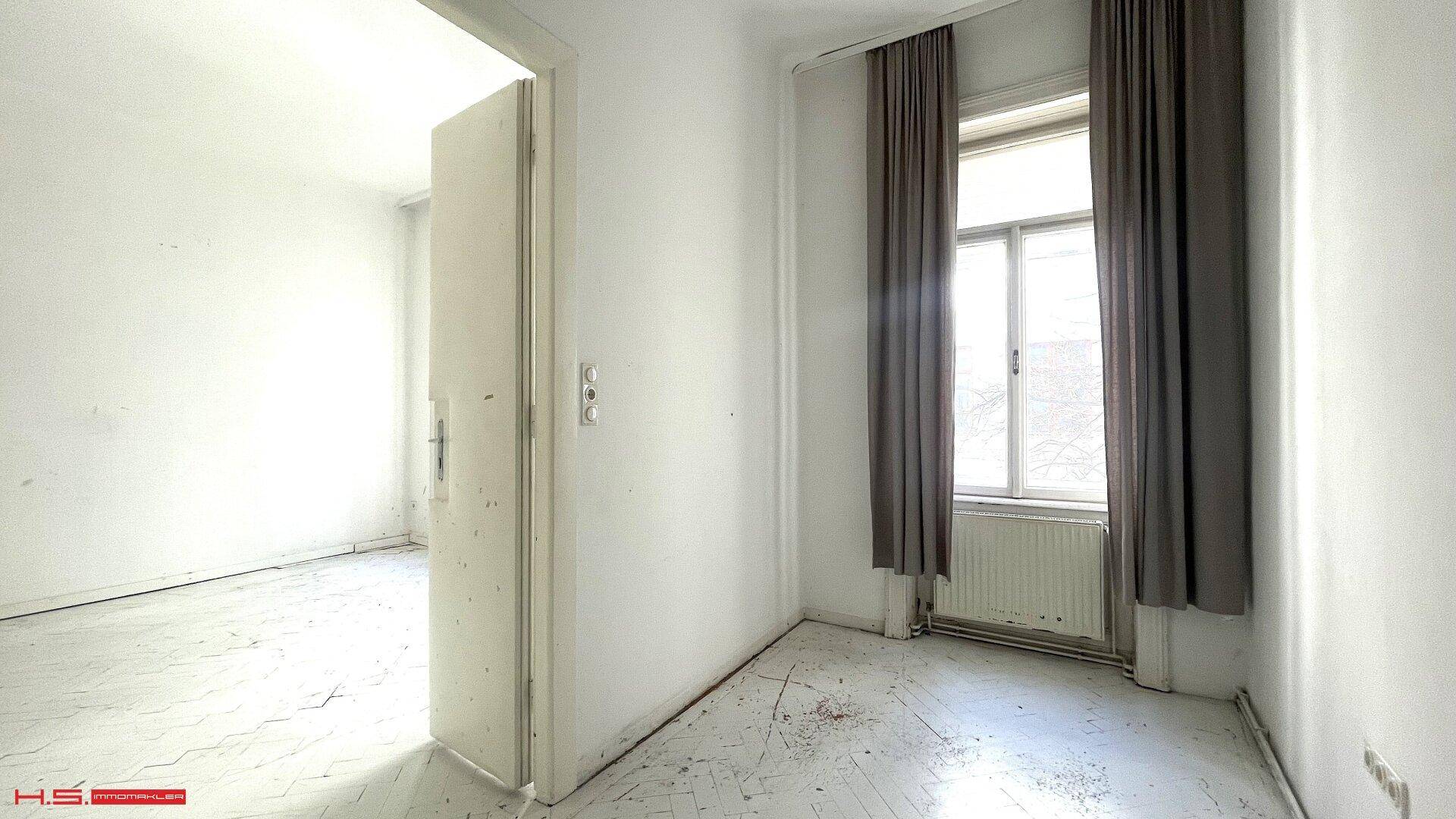 Lichtdurchflutetes Zimmer mit hohen Fenstern, Heizkörpern und Blick nach draußen.