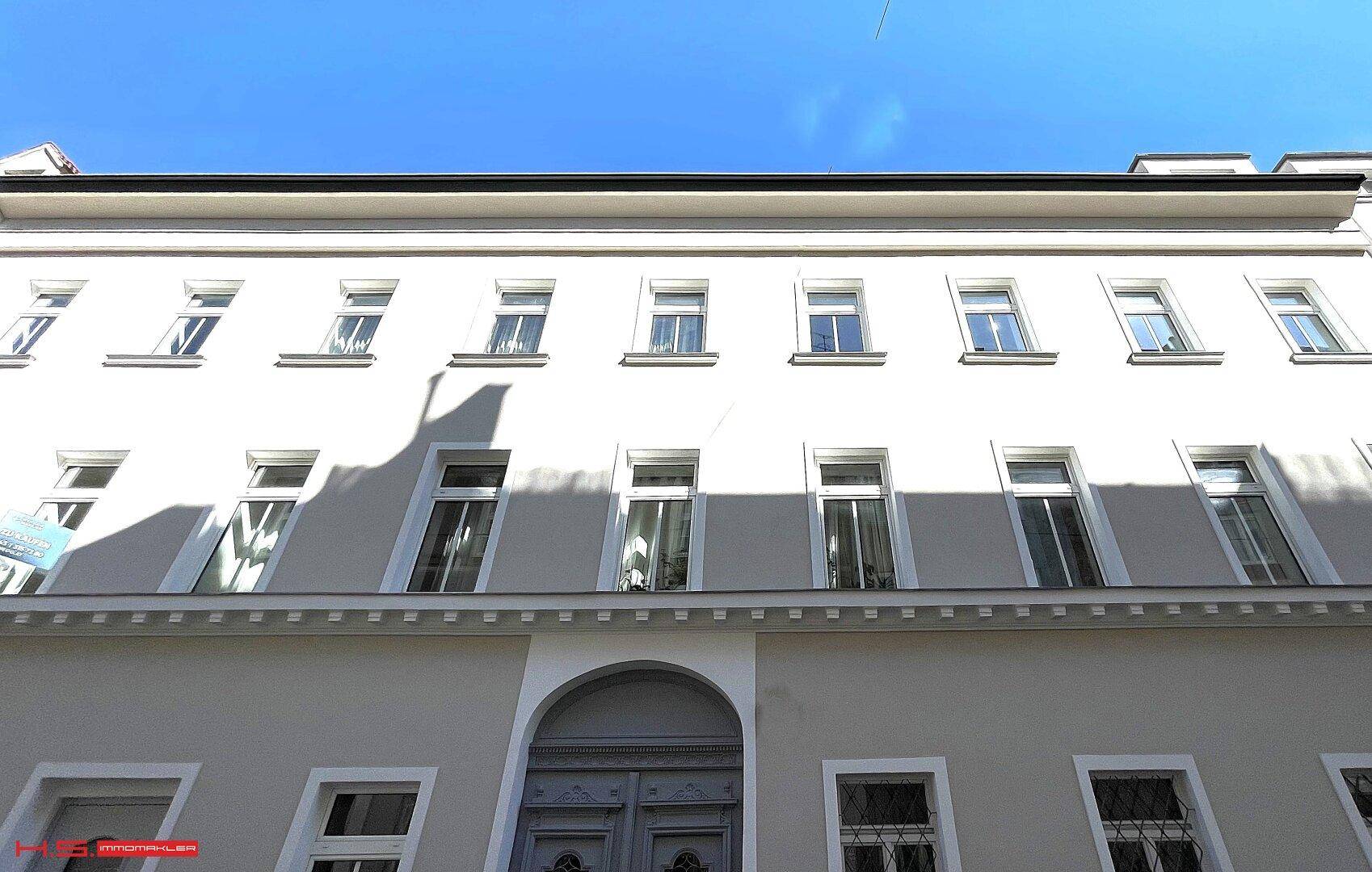 Klassische Gebäudefassade mit vielen Fenstern und einem hellen Anstrich unter blauem Himmel.