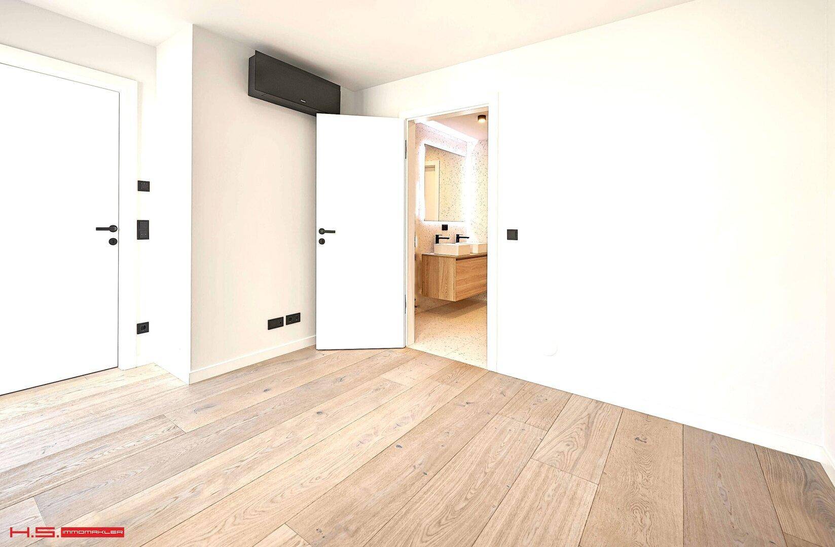 Geräumiges Zimmer mit Holzboden und offenem Zugang zu einem modernen Badezimmer.