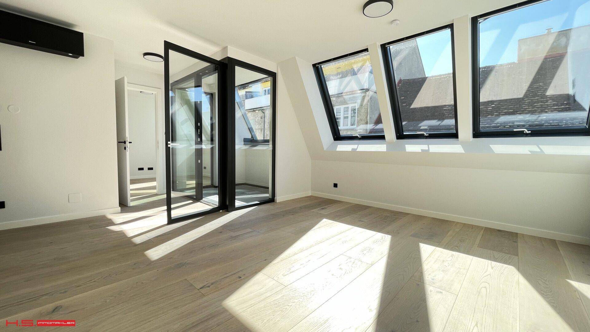 Geräumiges Wohnzimmer mit Holzboden, Dachfenstern und Zugang zum Balkon.