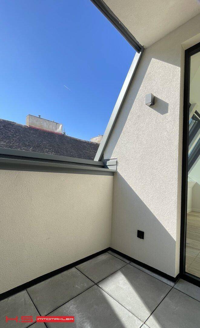 Kleiner, sonniger Balkon mit Fliesenboden und Blick auf die umliegenden Dächer.