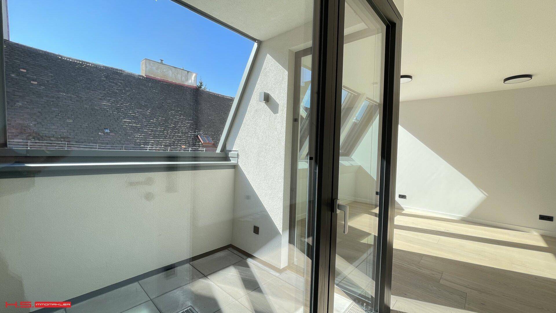 Kleiner Balkon mit Fliesenboden und Blick über die Dächer der Stadt unter blauem Himmel.