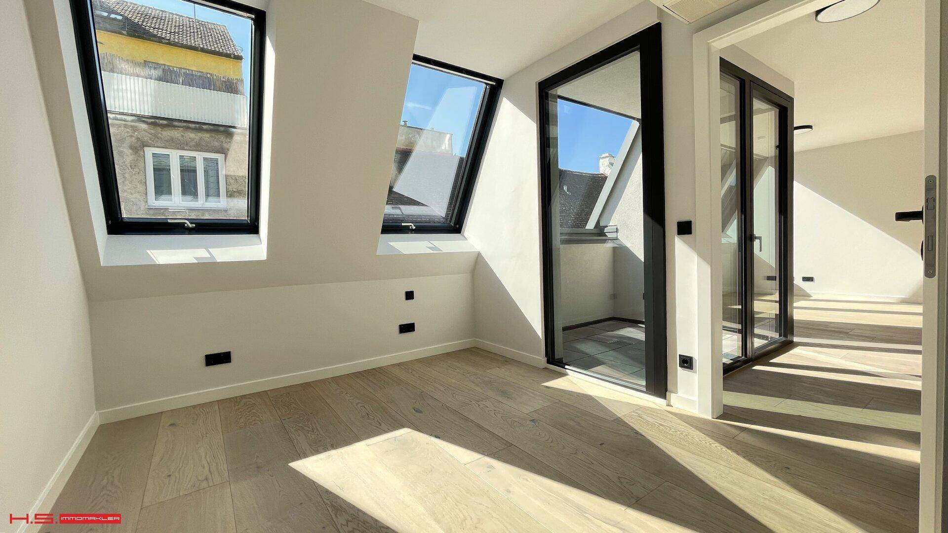 Helles Zimmer im Dachgeschoss mit Holzboden und schrägen Dachfenstern.