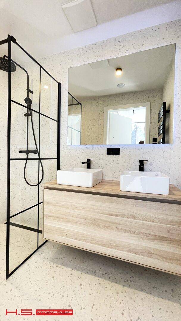 Modernes Badezimmer mit Doppelwaschbecken, großer Dusche und beleuchtetem Spiegel.