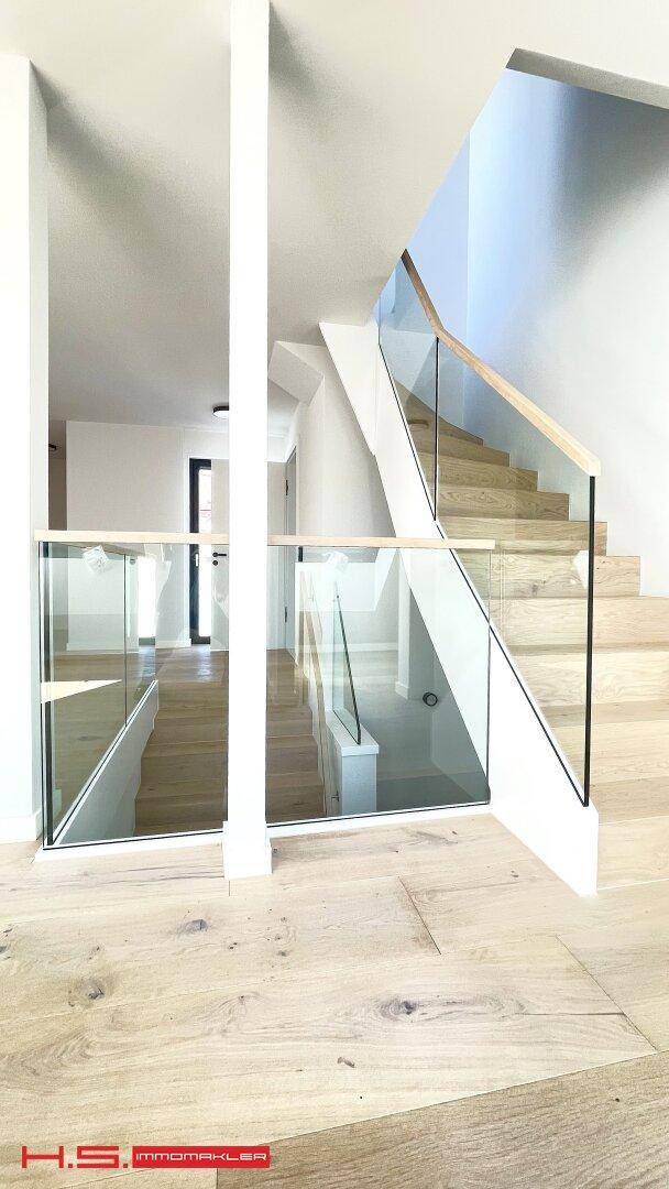 Heller Treppenbereich mit Glasgeländer und Eichenparkett, der verschiedene Ebenen des Hauses verbindet.