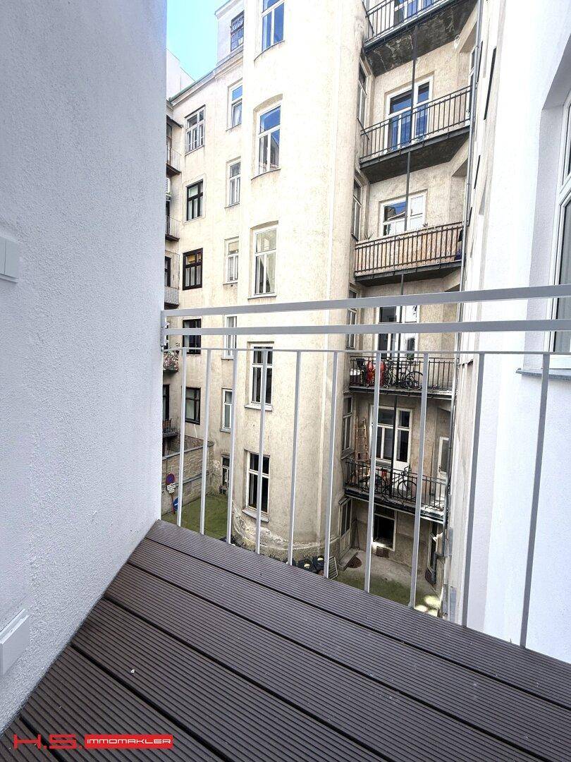 Kleiner Balkon mit Holzboden und Blick auf den Innenhof des Gebäudes.