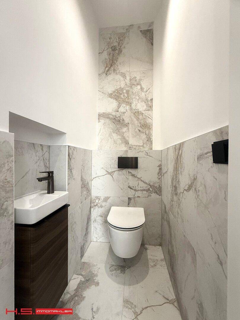 Modernes Gäste-WC mit Marmorfliesen, wandmontierter Toilette und kleinem Waschbecken.