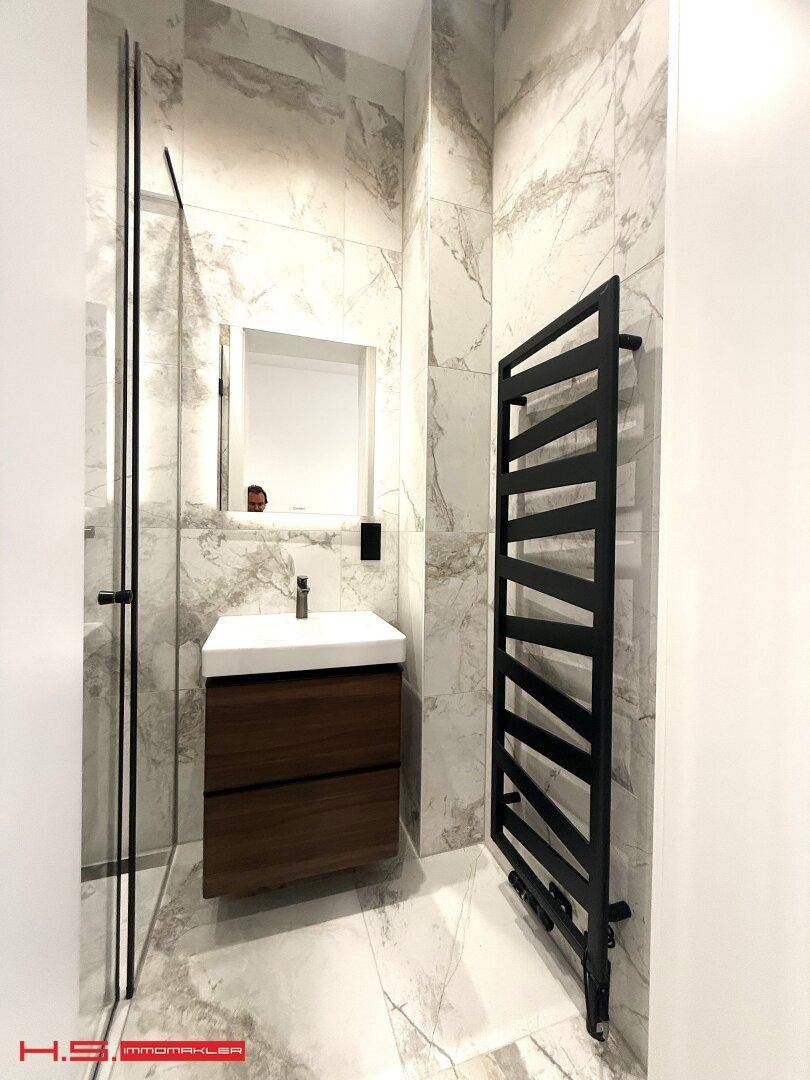 Modernes Badezimmer mit Marmorfliesen, Einzelwaschbecken, ebenerdiger Dusche und Handtuchheizkörper.