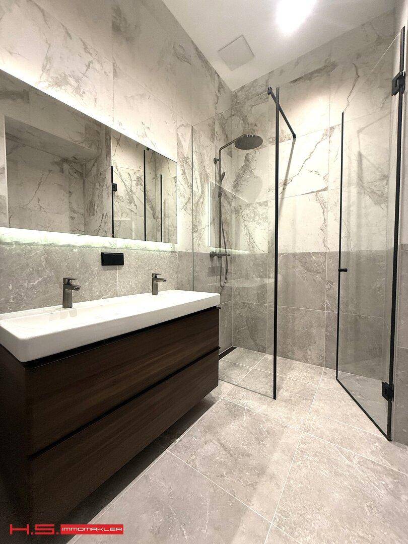 Modernes Badezimmer mit großformatigen Marmorfliesen, Doppelwaschbecken und ebenerdiger Dusche.