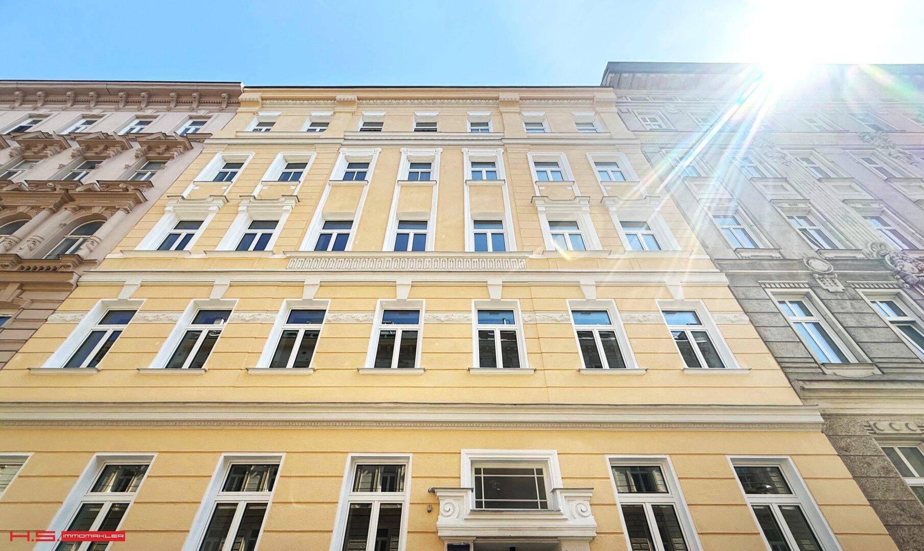 Sonnige Fassade eines eleganten Altbaus in der Stadt, frisch renoviert mit gelbem Anstrich und klassischen Details.
