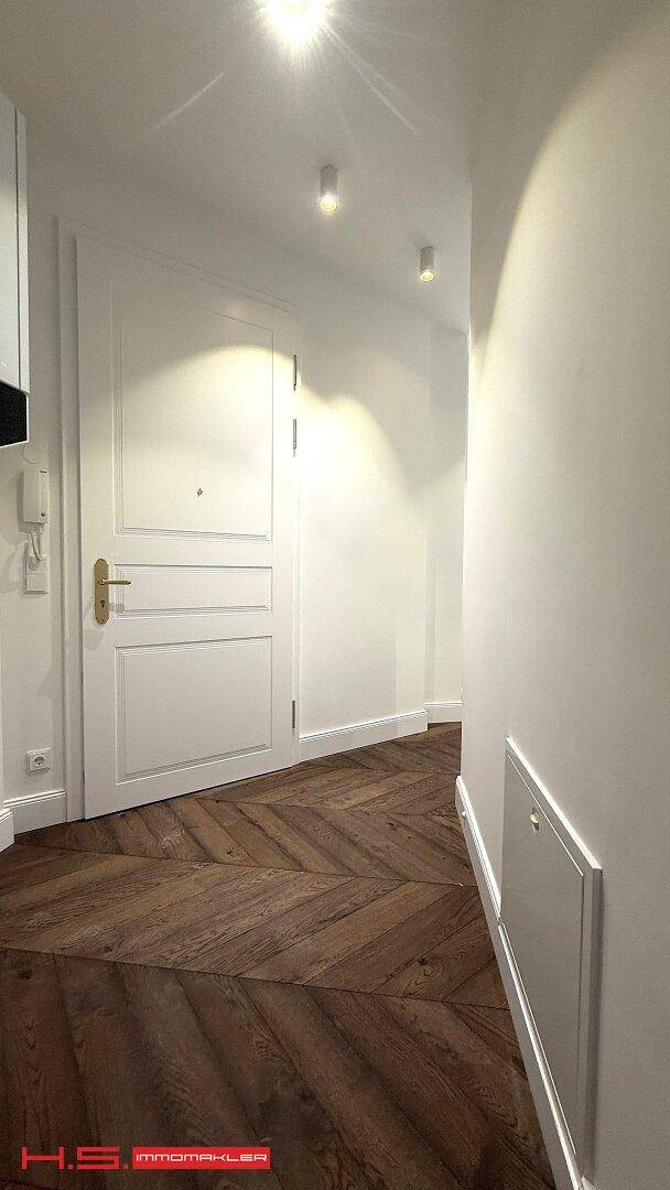 Heller Flur mit Fischgrätparkett und weißer Tür, gut beleuchtet.