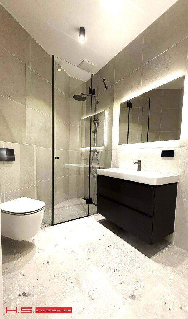 Modernes Badezimmer mit begehbarer Dusche, Wand-WC und beleuchtetem Spiegel.