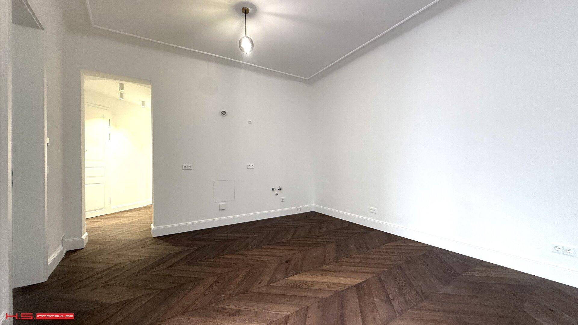 Heller Wohnraum mit elegantem Fischgrätparkett und schlichter Deckenleuchte.