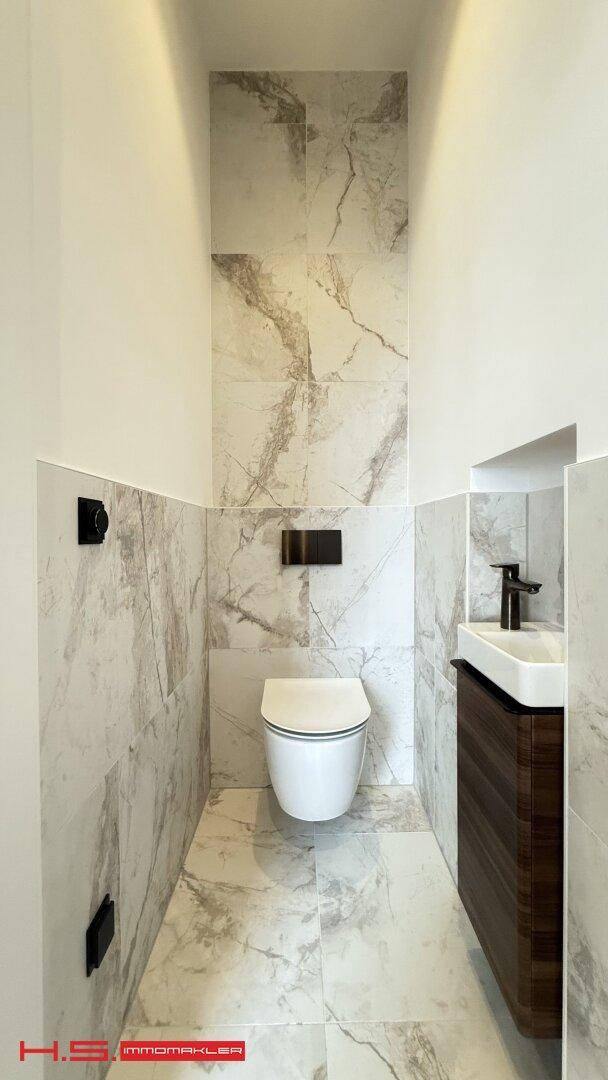 Modernes Gäste-WC mit eleganten Marmorfliesen, wandhängendem WC und kleinem Waschbecken für Besucher.