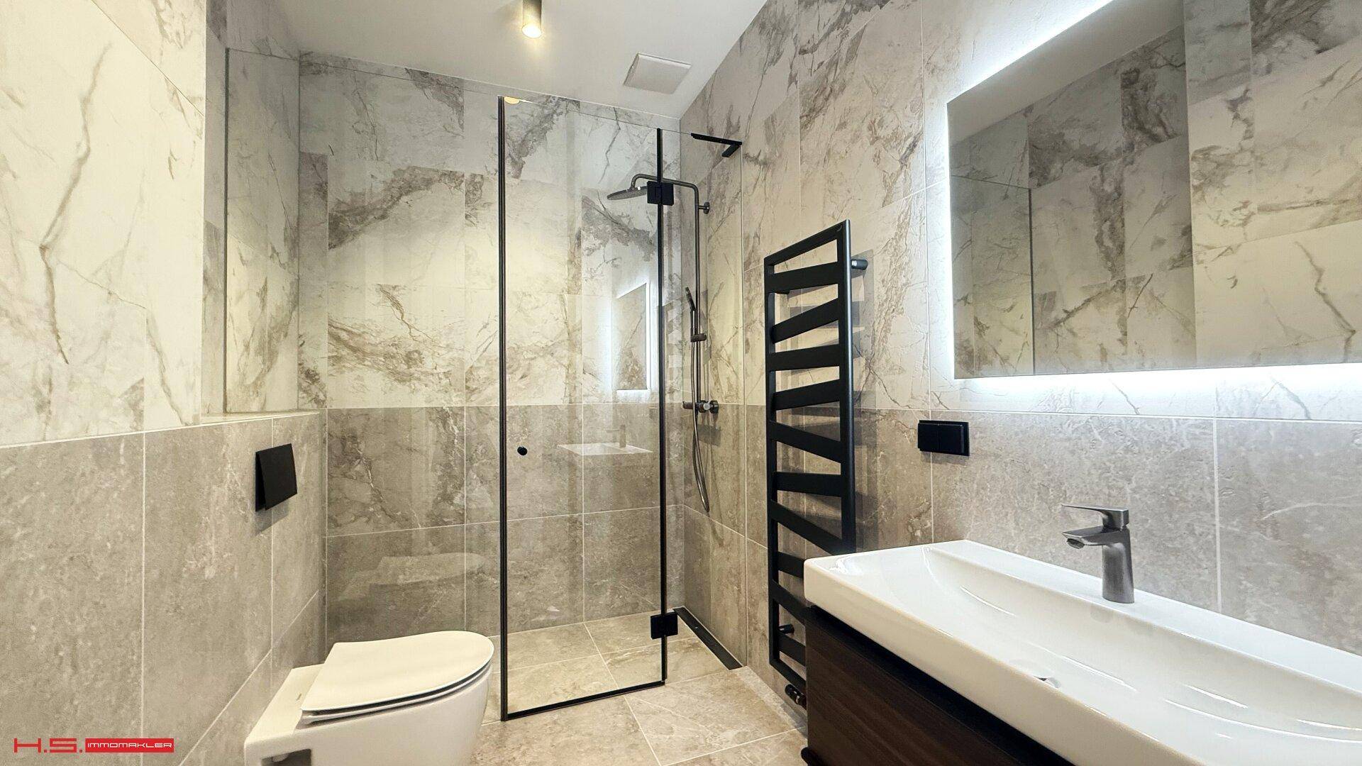Modernes Badezimmer mit großformatigen Fliesen, begehbarer Dusche und beheiztem Handtuchhalter für höchsten Komfort.