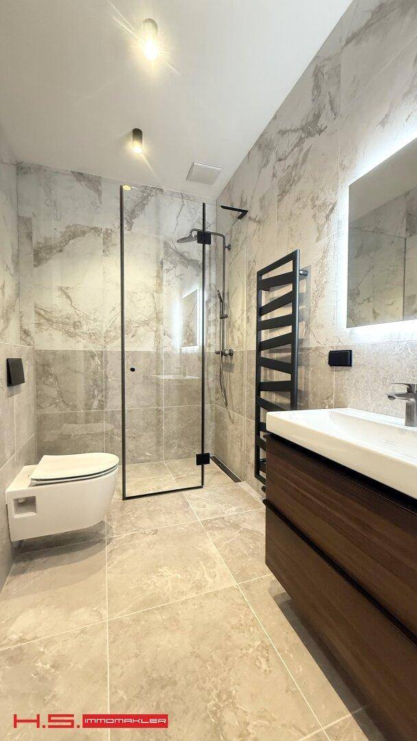 Stilvolles Badezimmer mit begehbarer Dusche, wandhängendem WC und modernem Waschtisch, alles in hochwertigen Materialien.