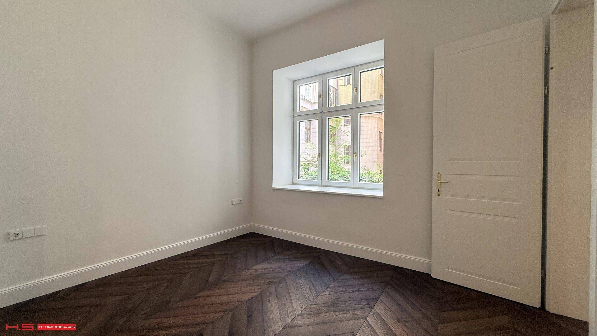 Gemütliches Zimmer mit Fischgrätparkett und einem großen Fenster, ideal als Schlafzimmer oder Arbeitsbereich.
