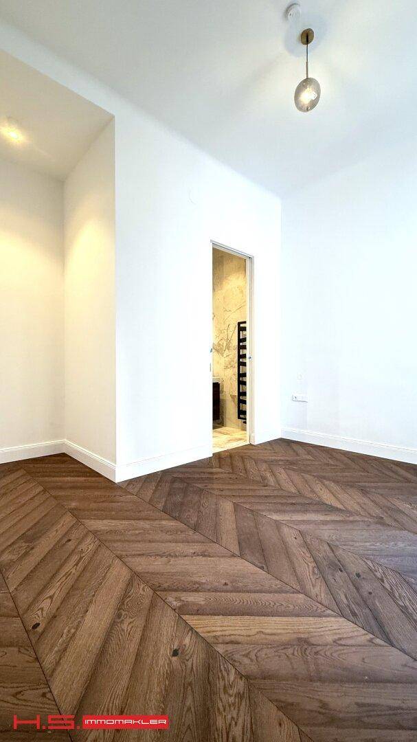 Geräumiger, heller Raum mit Fischgrätparkett und Zugang zu einem modernen Badezimmer, ideal für entspannte Stunden.