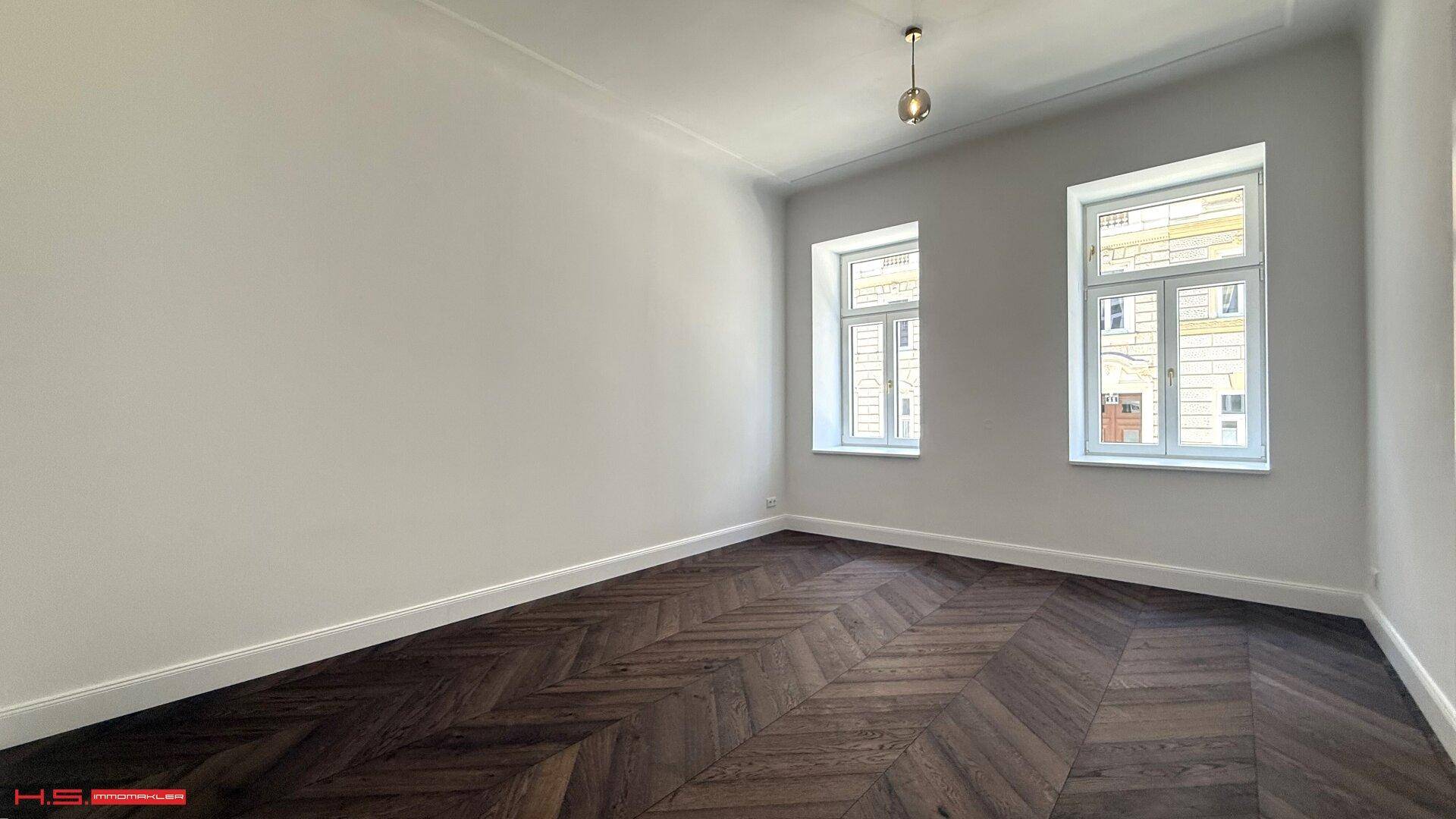 Geräumiges Zimmer mit Fischgrätparkett und zwei großen Fenstern, ideal für Wohnzwecke und vielseitig gestaltbar.