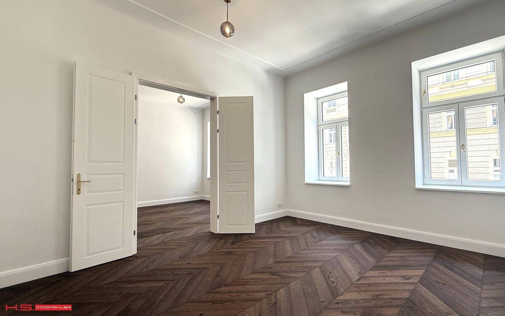 Helles Zimmer mit elegantem Fischgrätparkett und hohen weißen Türen, das viel natürliches Licht erhält.