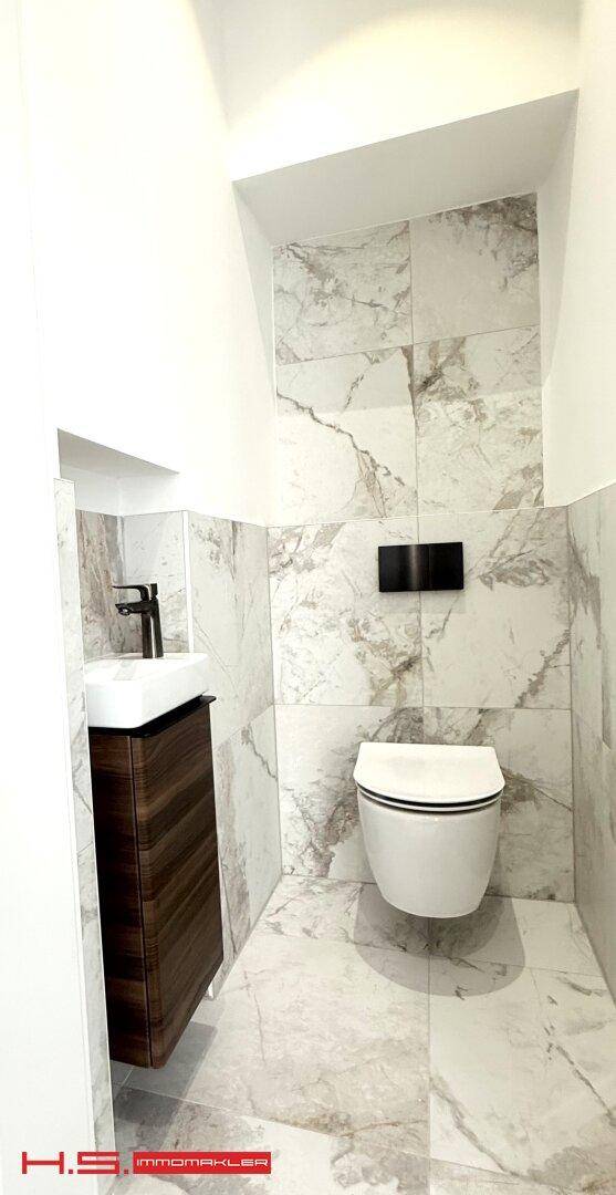 Modernes Gäste-WC mit wandhängendem WC, kleinem Waschtisch und eleganten Marmorfliesen.