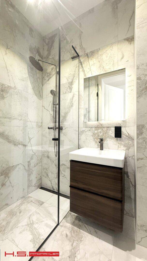 Helles Badezimmer mit modernem Waschtisch, begehbarer Dusche und großformatigen Marmorfliesen.