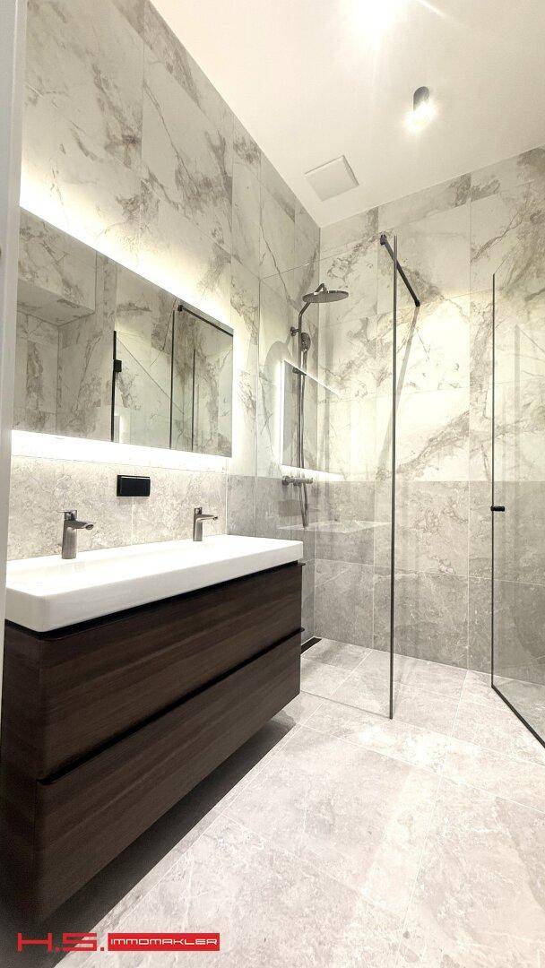 Elegantes Badezimmer mit Doppelwaschbecken, beleuchtetem Spiegel und geräumiger begehbarer Dusche.