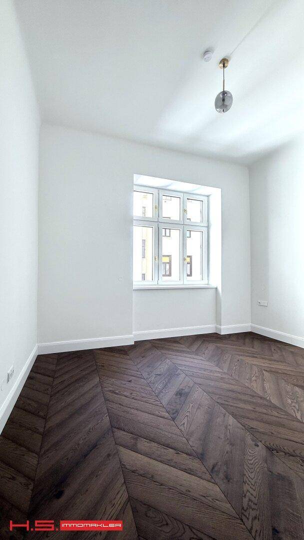 Helles Zimmer mit dunklem Fischgrätparkett und einem Fenster, das den Raum mit Tageslicht füllt.