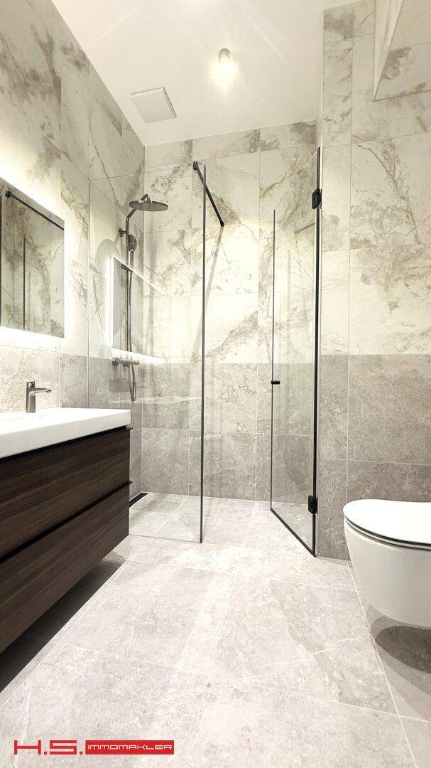Modernes Badezimmer mit begehbarer Dusche, wandhängendem WC und eleganten Marmorfliesen.
