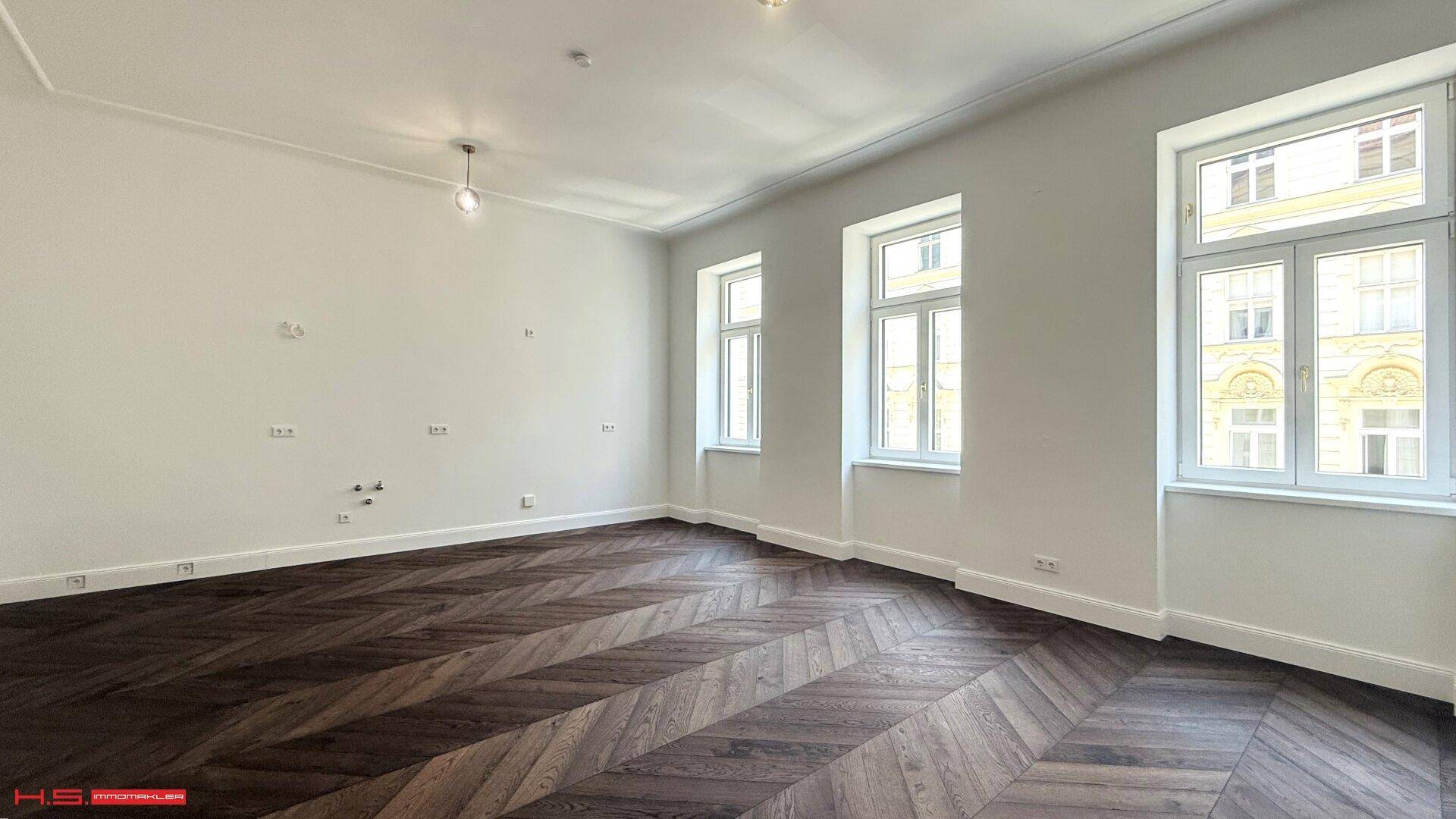 Geräumiges, helles Zimmer mit elegantem Fischgrätparkett und hohen Fenstern, bereit zur Einrichtung.