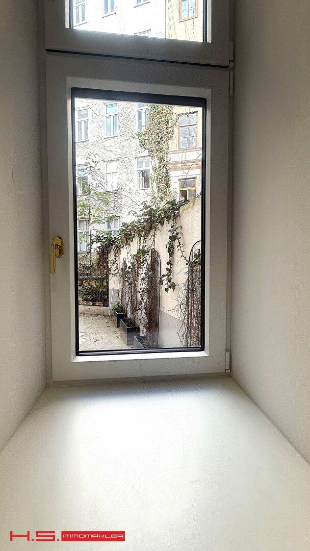 Fenster mit Blick auf einen begrünten Innenhof, der Ruhe verspricht.