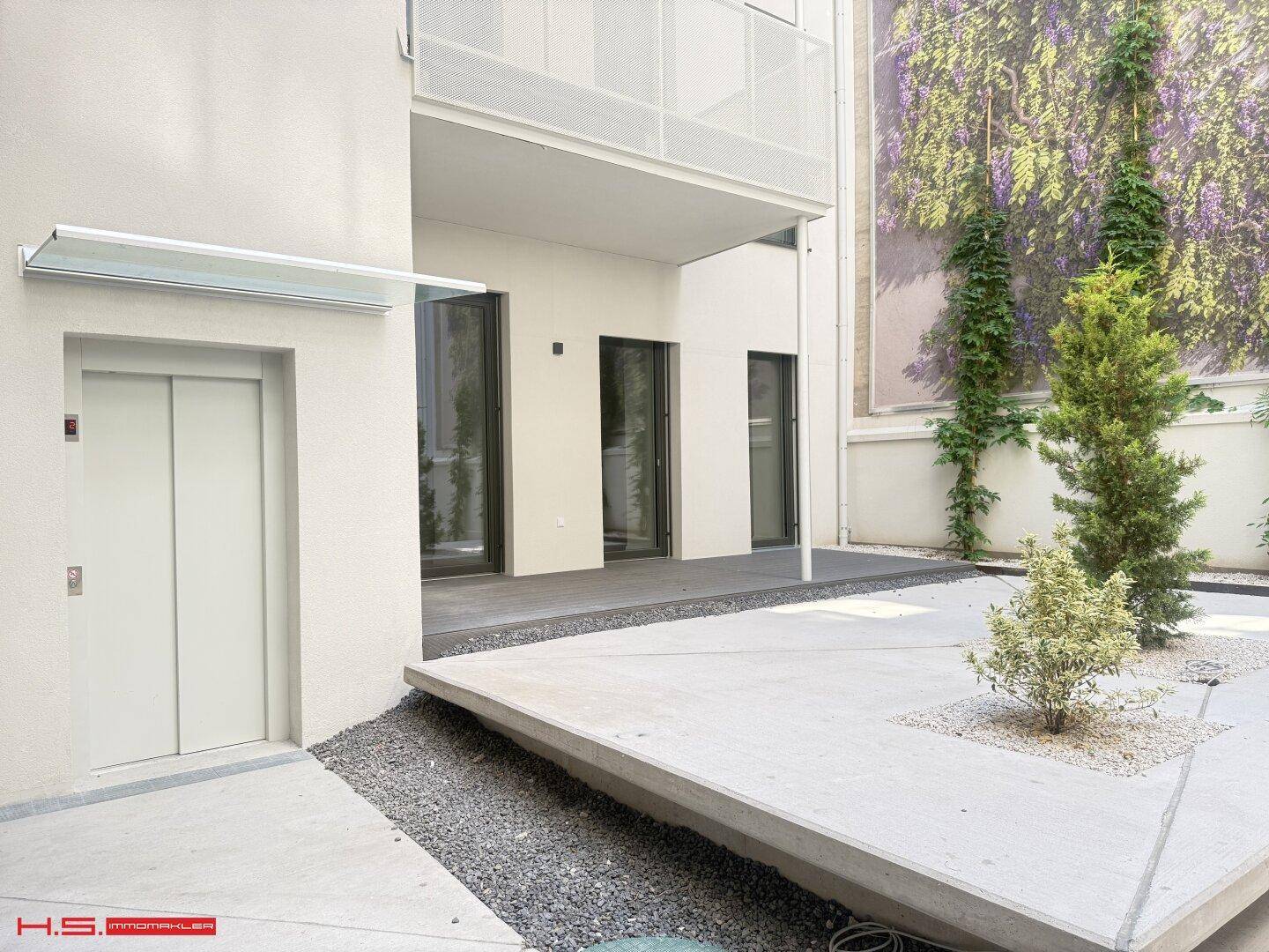 Moderner Außenbereich mit Aufzugzugang, begrünten Wänden und einer gestalteten Terrasse.