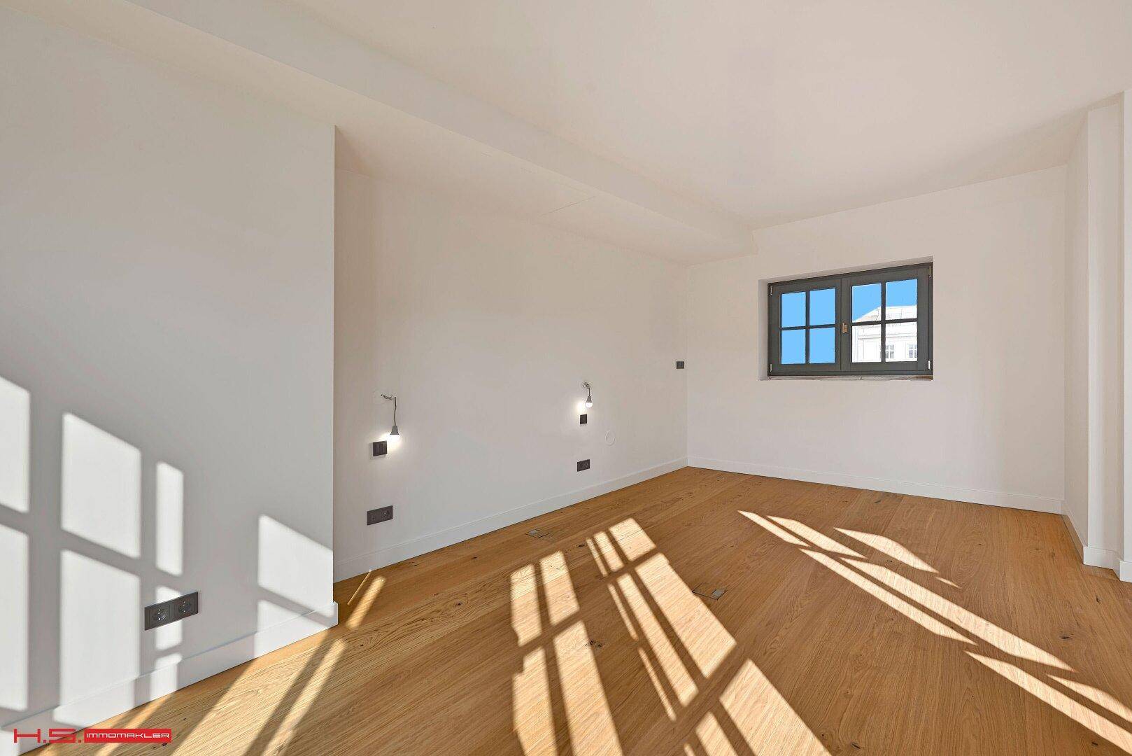 Helles Zimmer mit Holzboden und einem Fenster, das viel natürliches Licht in den Raum bringt.