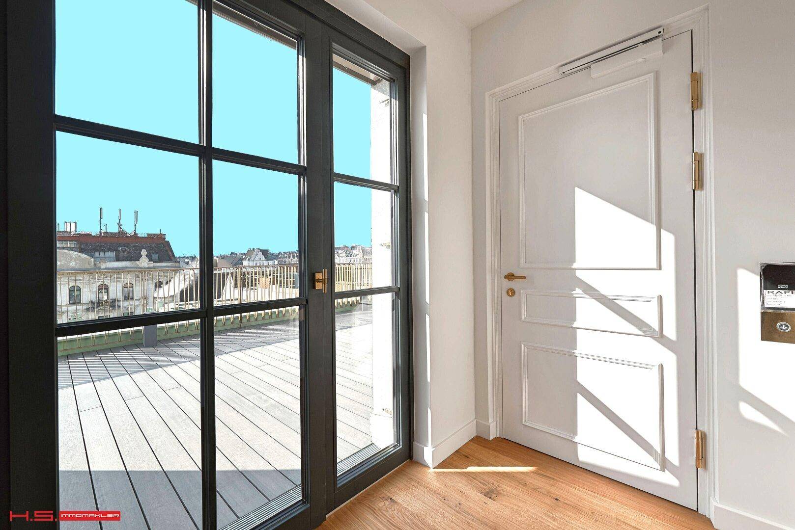 Eingangsbereich mit weißer Tür und großen Fenstertüren, die den Blick auf die Dachterrasse freigeben.