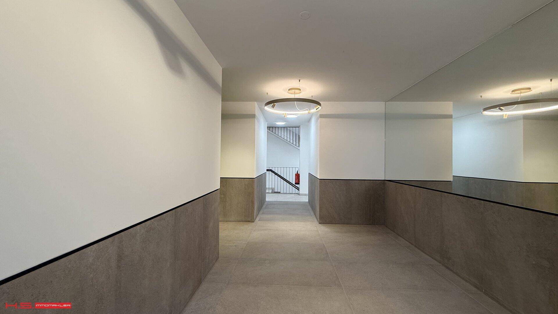 Moderner Flur mit grauen Fliesen, einer Spiegelwand und indirekter Beleuchtung, die zu den Treppen führt.