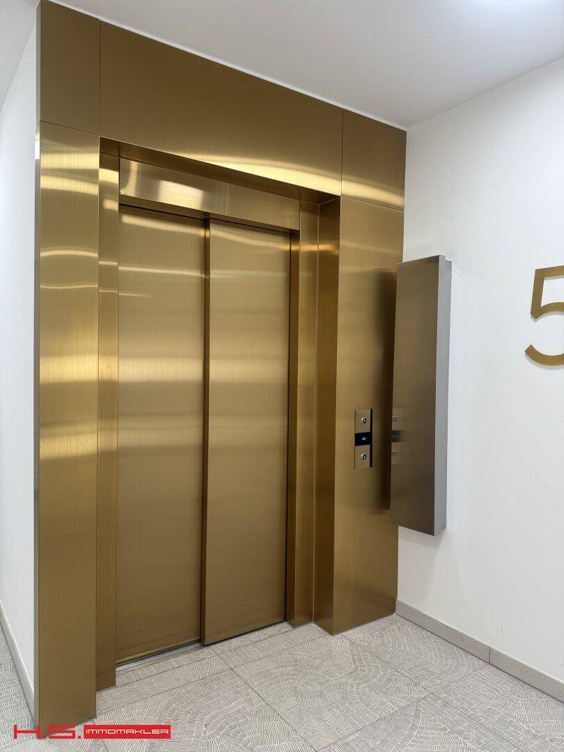 Eleganter Aufzug mit goldener Tür in einem modernen Flur, der Zugang zu den oberen Etagen bietet.